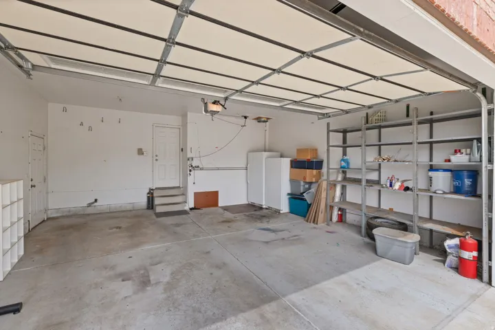 Spacious garage featuring a concrete floor, overhead garage door, built-in shelving, two entry doors, and a garage door opener