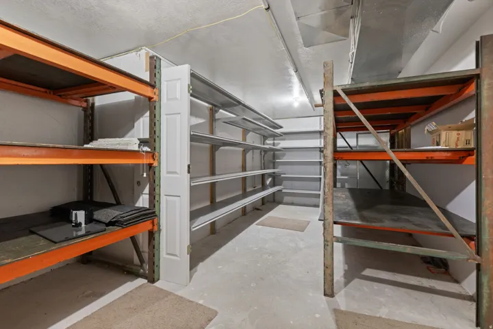 Storage room featuring concrete flooring, exposed overhead ductwork, and abundant shelving