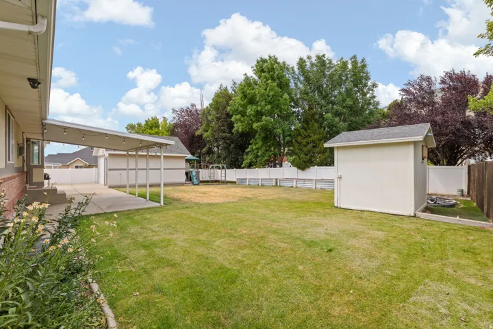 Expansive backyard featuring a covered patio with string lighting, a large storage shed, and a privacy fence