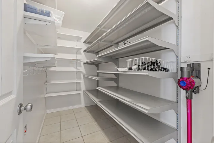 Walk-in pantry featuring white shelving, tile flooring, and a white door with a satin nickel doorknob