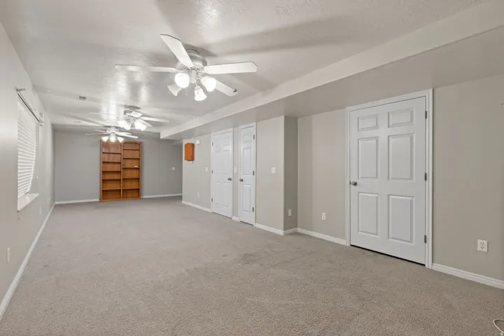 Spacious room featuring neutral carpet flooring, light gray wall paint, multiple ceiling fans with integrated lighting, and white six-panel doors