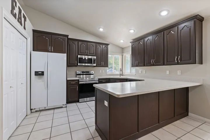 Kitchen featuring dark wood cabinetry, white stone countertops, stainless steel appliances, and tile flooring