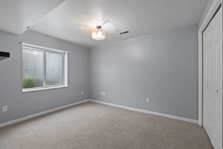Carpeted room featuring a white-trimmed window, light gray walls, a flush-mount ceiling light fixture, and a bi-fold closet door