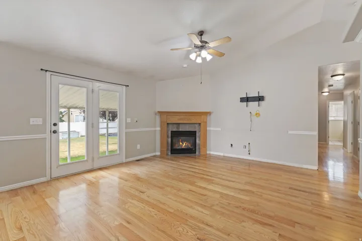 Spacious living area featuring light wood-finish flooring, a corner fireplace with a wood mantel, and double French doors opening to the exterior