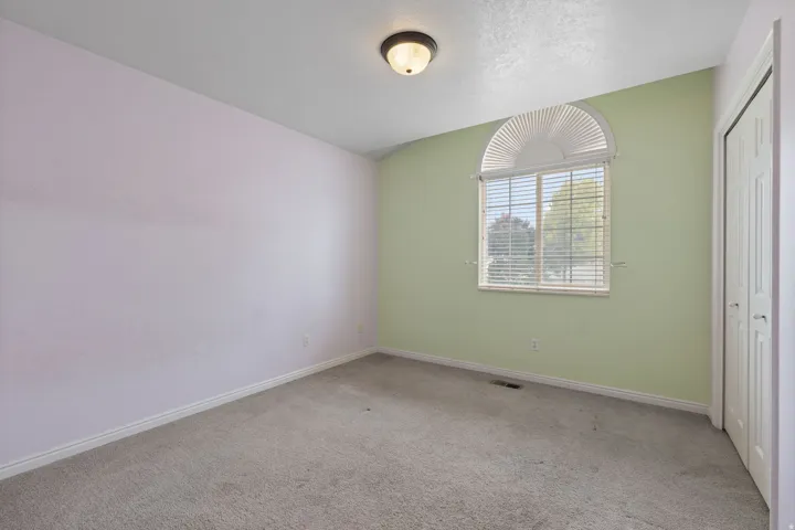 Room featuring a prominent arched window with horizontal blinds, neutral carpet, and a bi-fold closet door