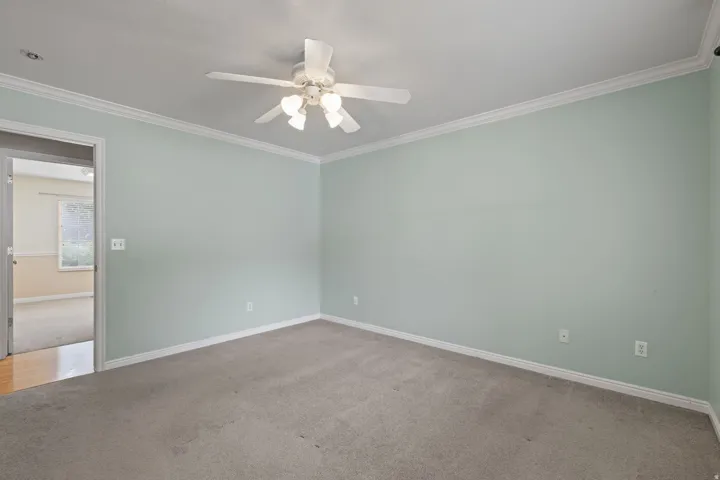 Carpeted room featuring a ceiling fan with integrated lighting, crown molding, and baseboards