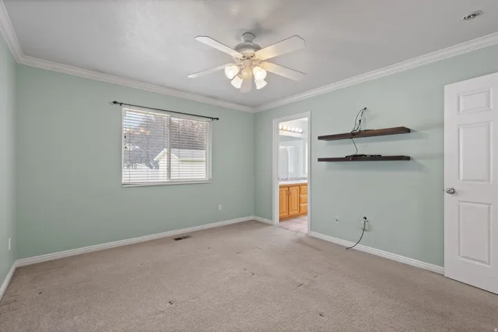 Carpeted room featuring a ceiling fan with integrated lighting, crown molding, and a window with horizontal blinds