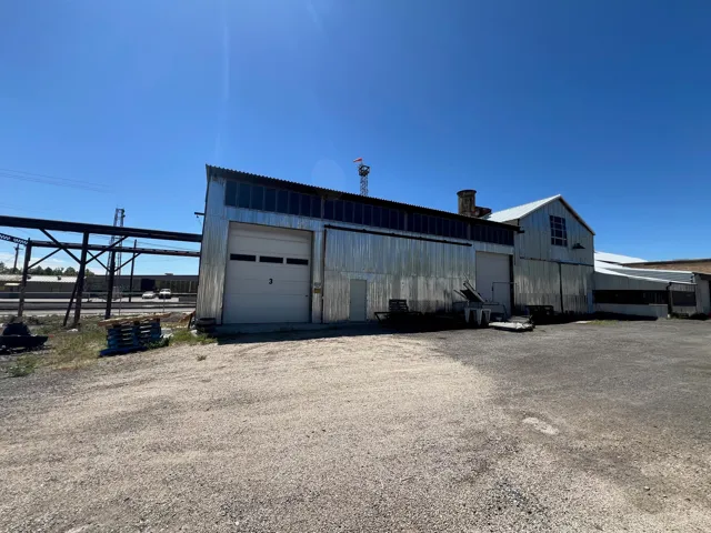 Industrial building featuring corrugated metal siding, multiple roll-up doors, and a gravel lot