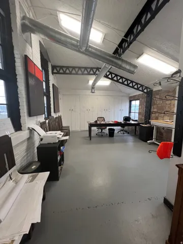 Spacious room featuring exposed ductwork, skylights, white painted brick walls, a built-in storage wall, and a stone accent wall