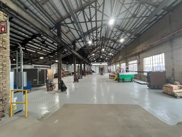 Expansive industrial interior featuring a high-pitched roof with exposed steel trusses and abundant natural light from numerous multi-pane windows