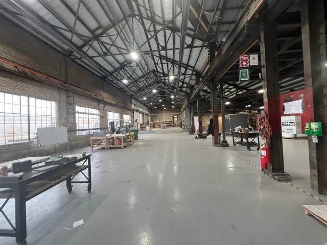 Spacious industrial interior featuring a high gabled ceiling with exposed metal trusses and overhead lighting
