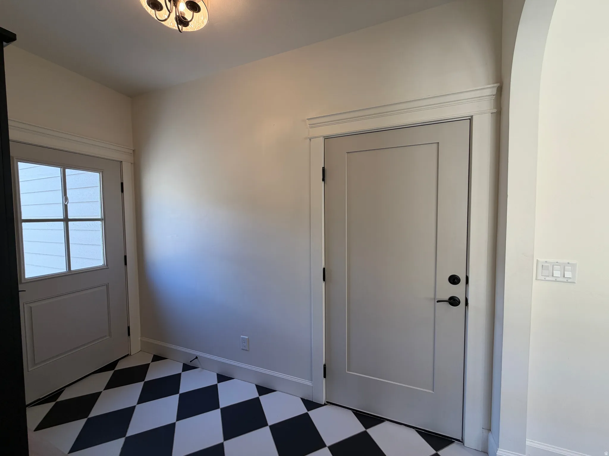 Entryway featuring black and white checkered flooring, a paneled door with black hardware, and an arched doorway
