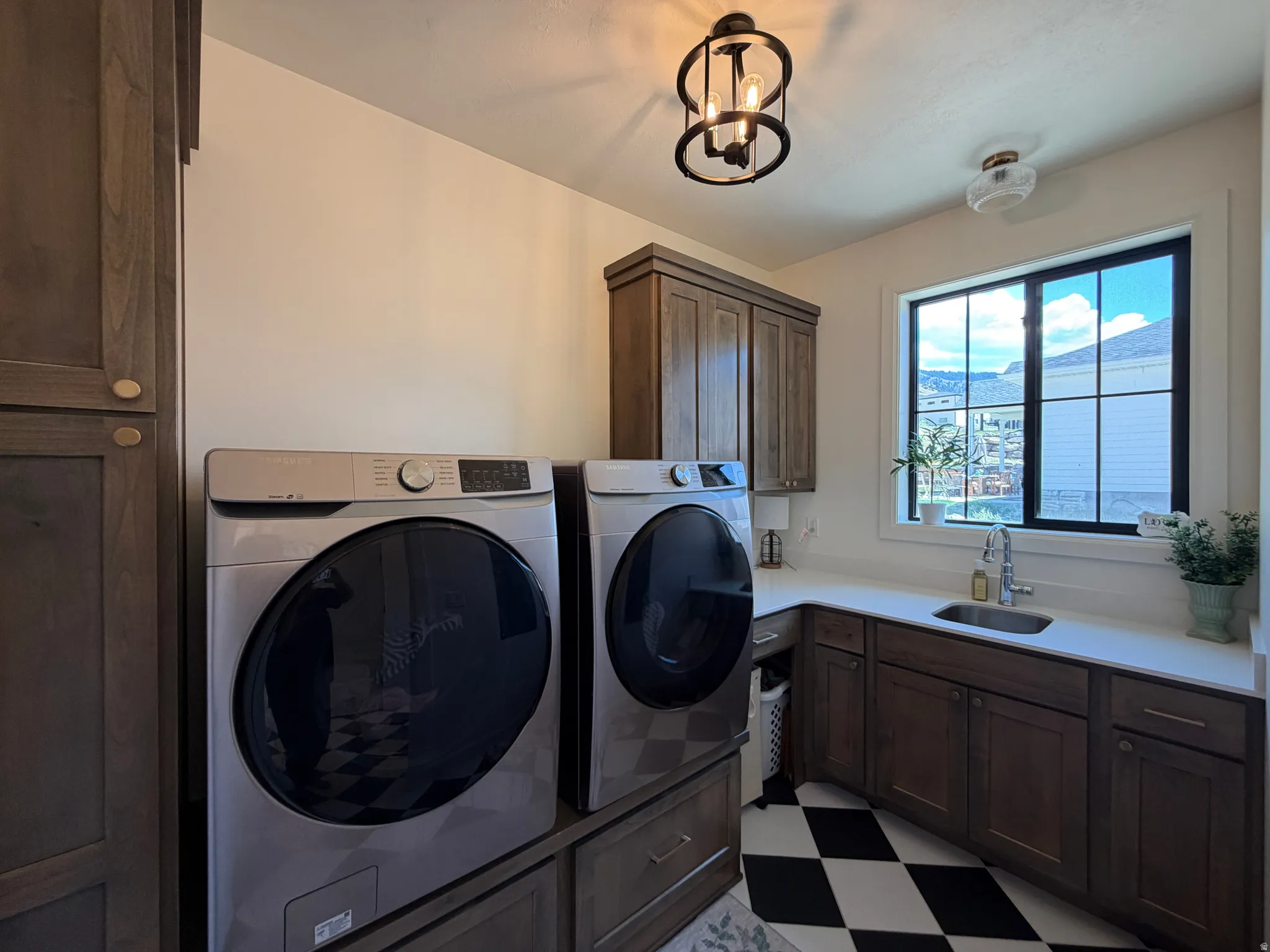 Laundry area featuring checkerboard flooring, dark wood-finish cabinetry, white countertops, and a stainless steel sink with a chrome faucet