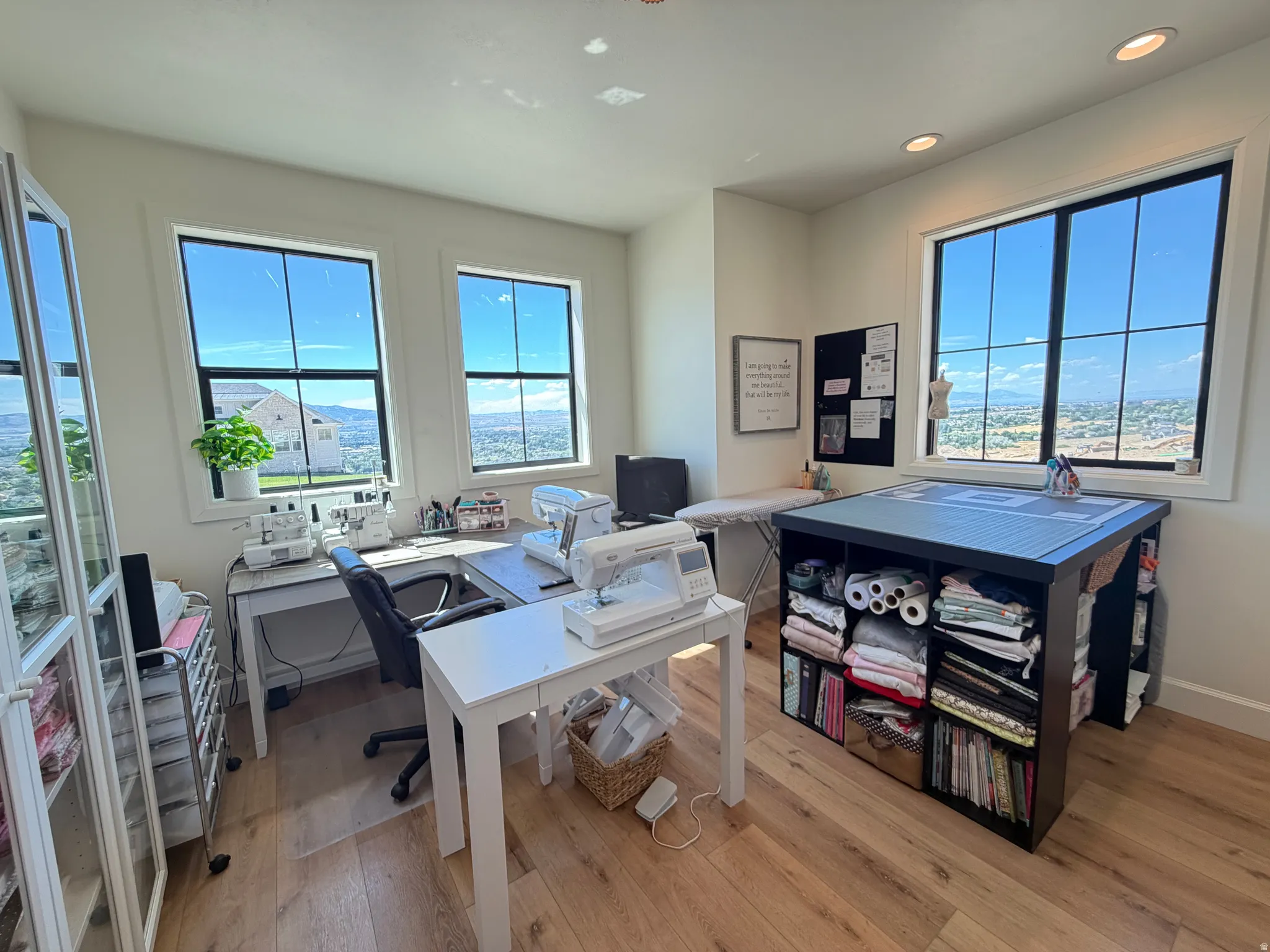 Bedroom 1, has a walk-in closet that now beeing used as a sewing studio . Bright room featuring multiple large windows with black grilles, wood-finish flooring, recessed lighting, and white walls