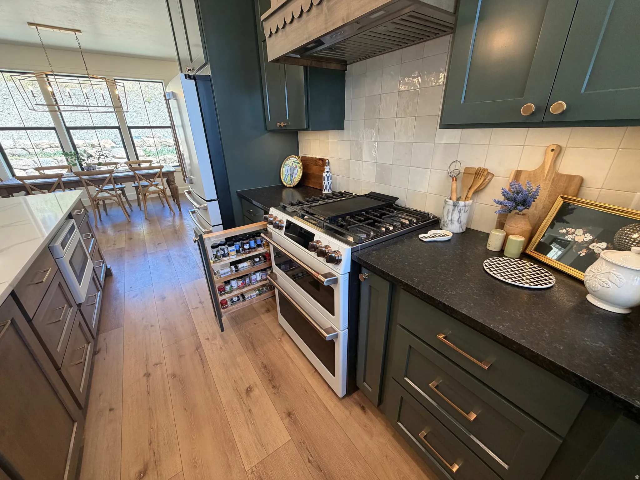 Gourmet kitchen featuring a stainless steel range with double ovens, dark green cabinetry with brass hardware, dark countertops, a white subway tile backsplash, and light wood-finish flooring