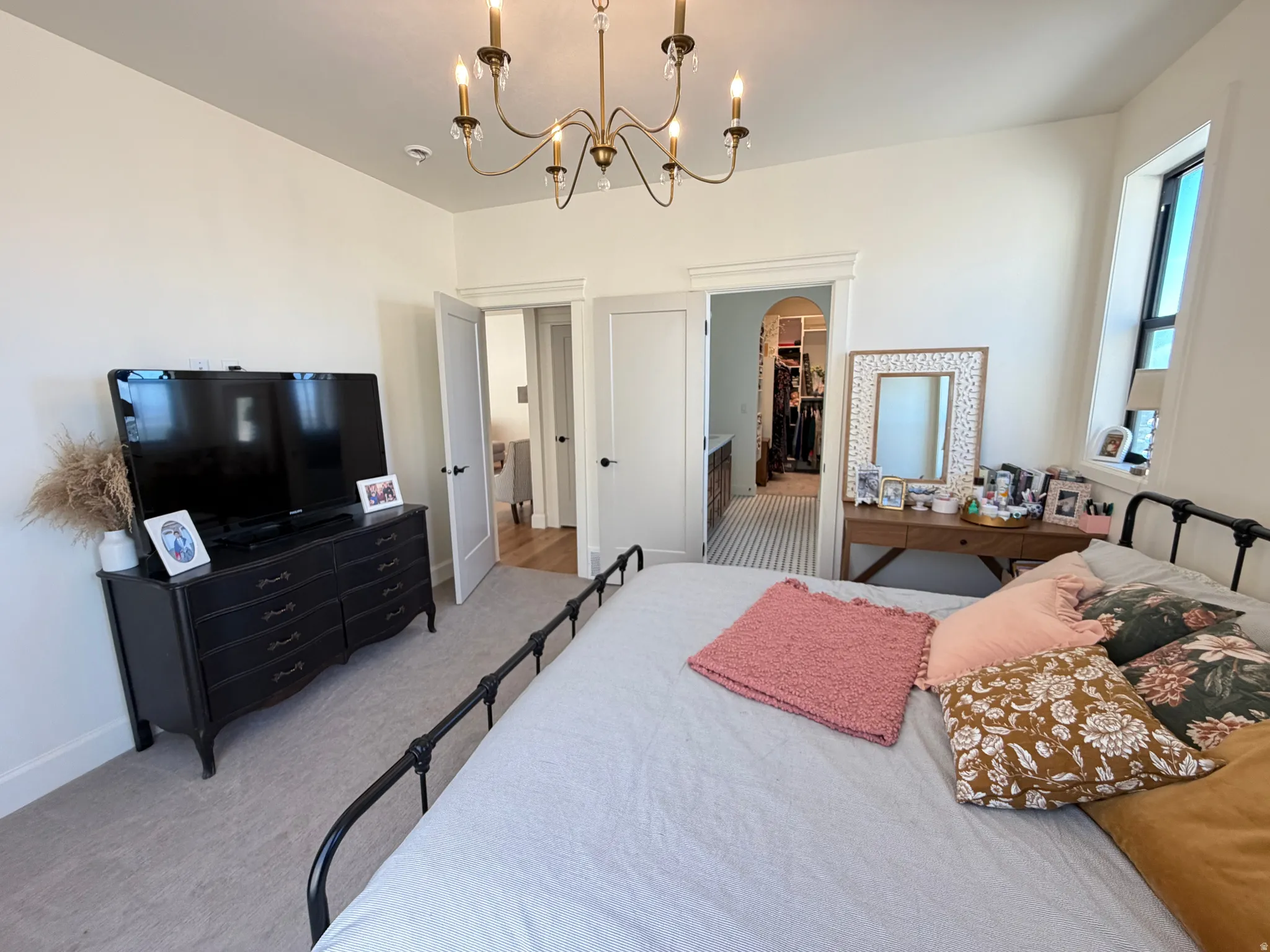 Primary Large Spacious room featuring a brass chandelier, light-colored walls, carpeted flooring, and a window with natural light