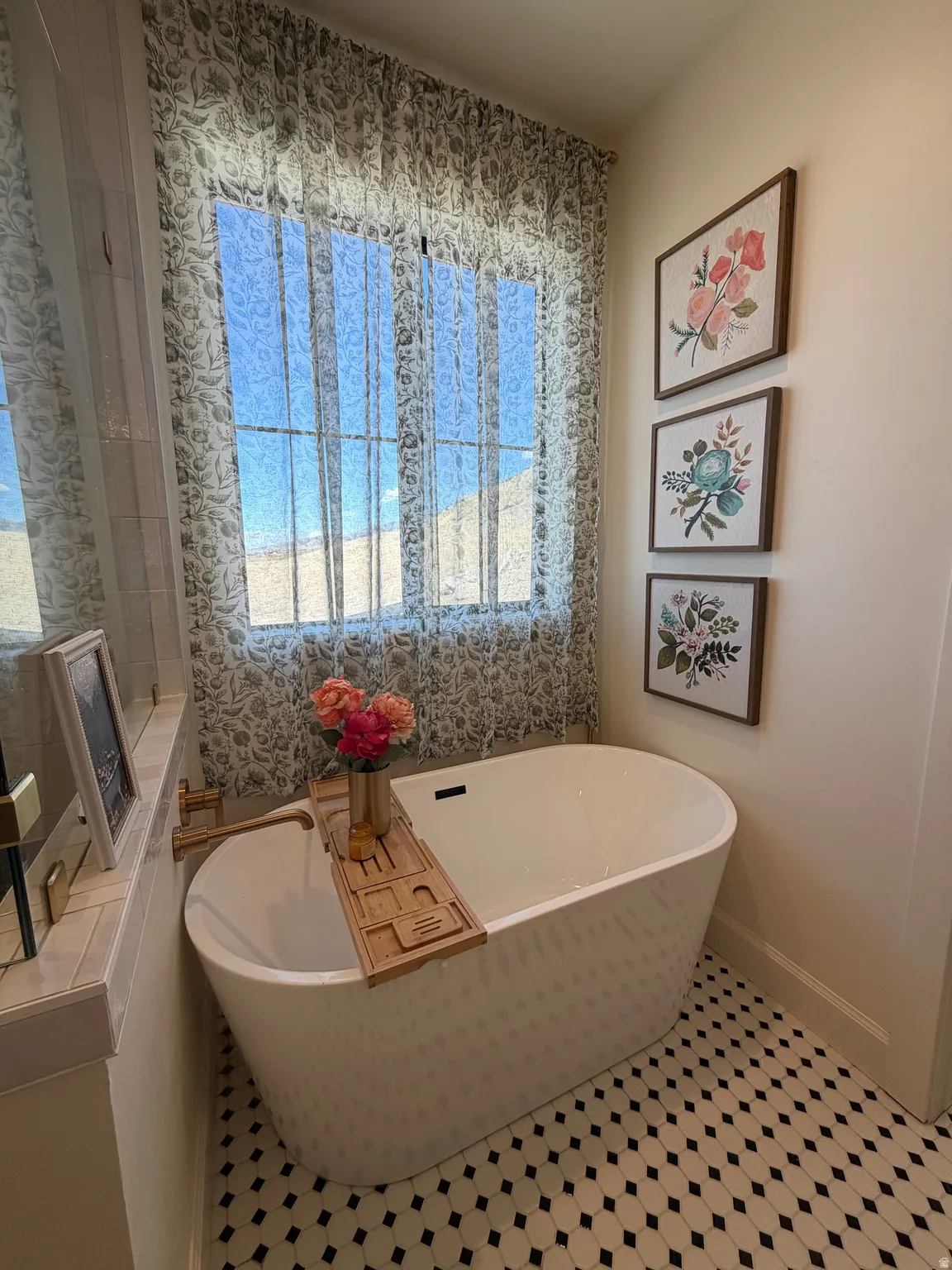 Freestanding soaking tub with a wall-mounted faucet, complemented by patterned sheer window treatments and hexagon tile flooring