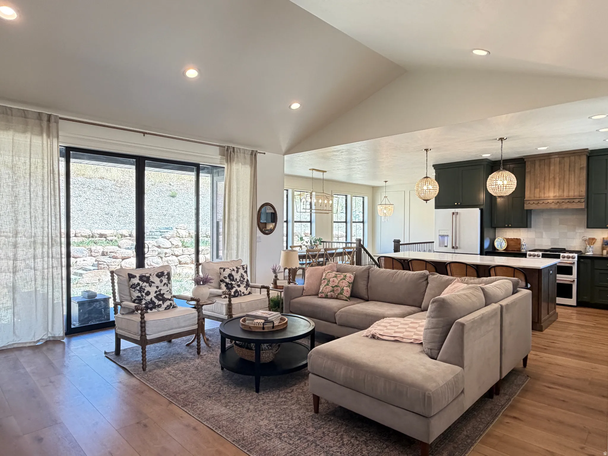Spacious living area featuring vaulted ceilings, wood-finish flooring, and a large sliding glass door
