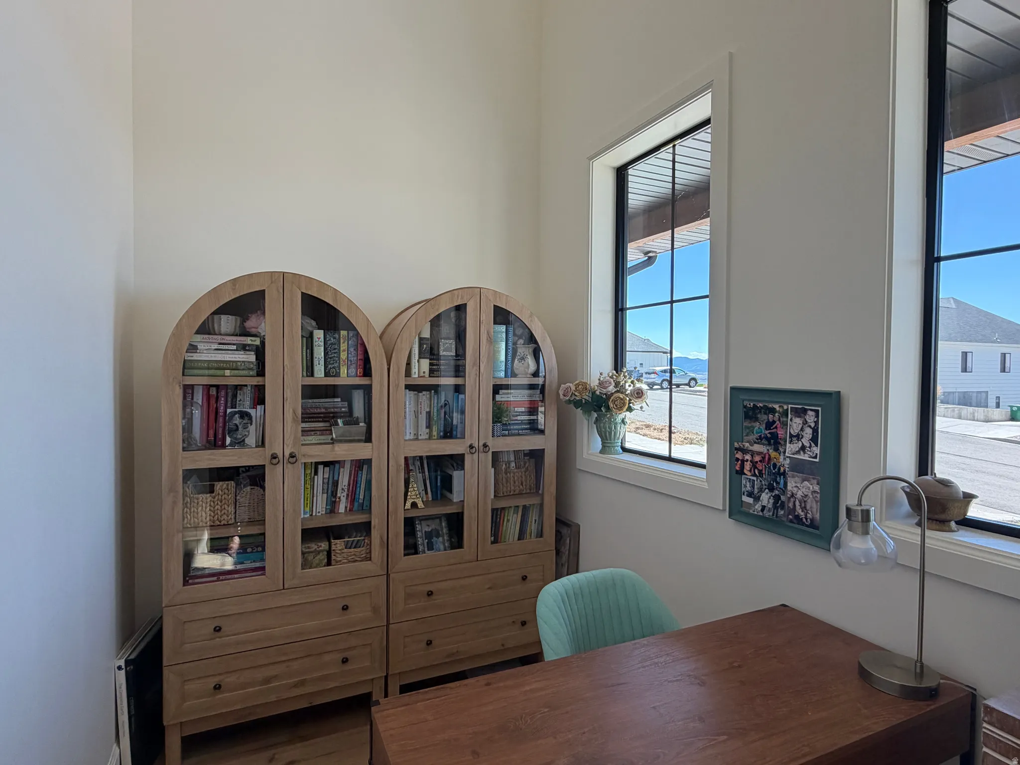 Room featuring two arched wood-finish display cabinets with glass doors, tall ceilings, and two large windows and a smaller window higher up with black framing and  decorative chandelier light/fan