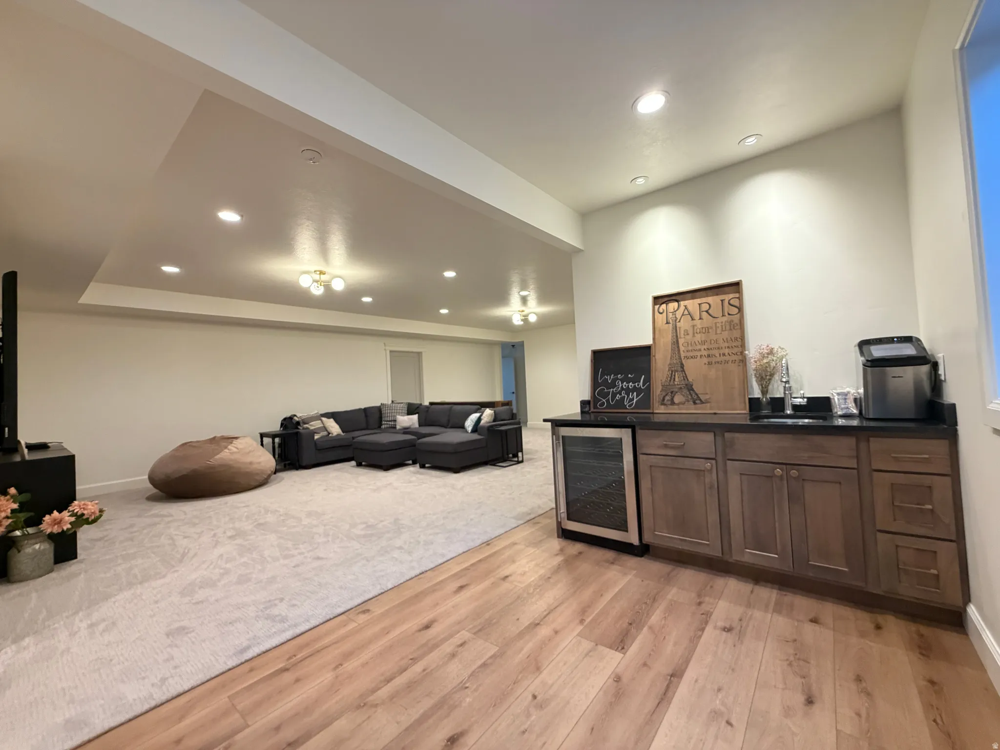 Lower-level entertainment space featuring wood-finish flooring, a built-in wet bar with dark countertops and wood cabinetry, recessed lighting, and a partial carpeted area