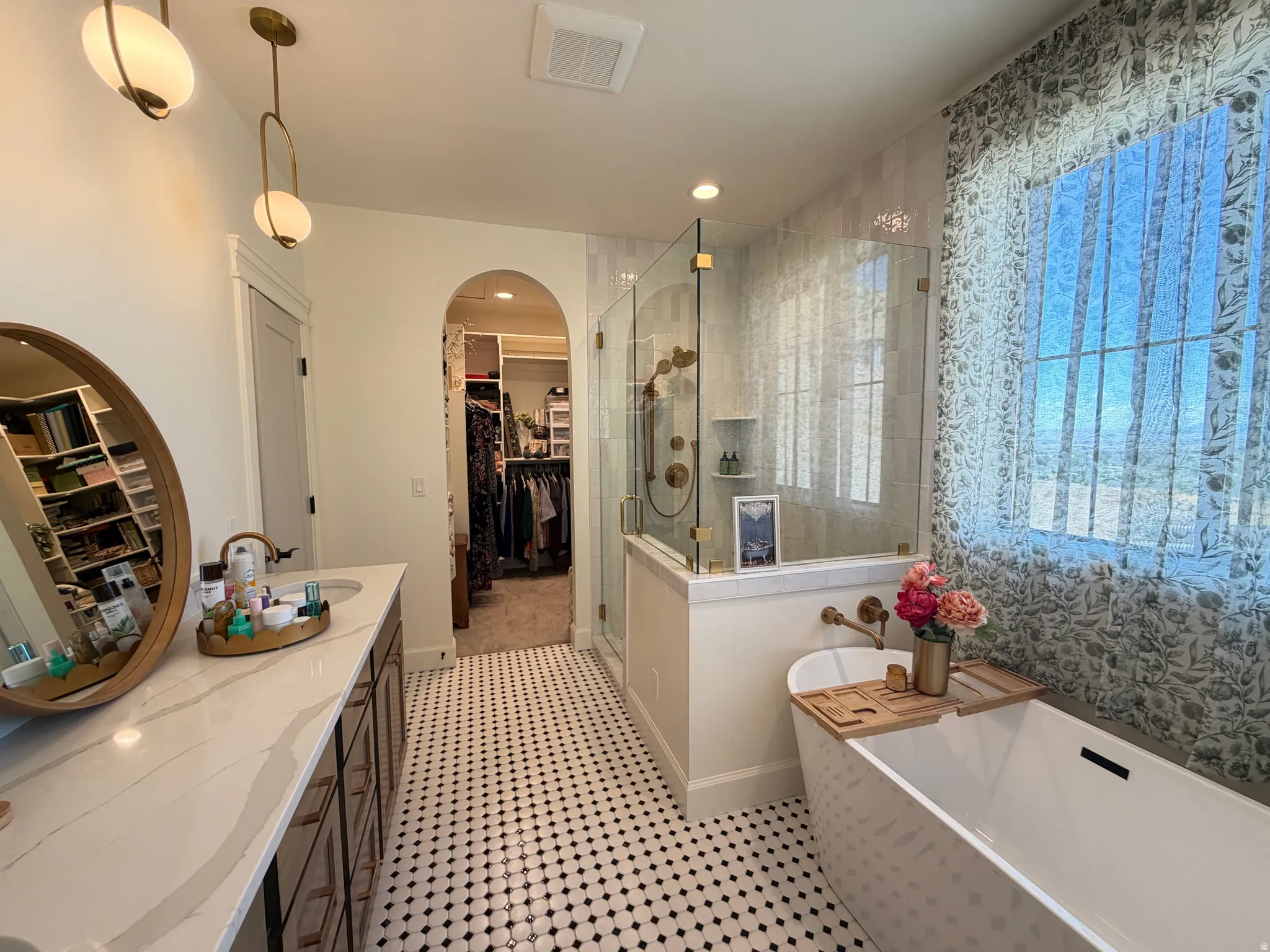 Bathroom featuring a freestanding soaking tub, a frameless glass shower enclosure, a dual vanity with a light-toned countertop, black and white hex tile flooring, and an arched entry