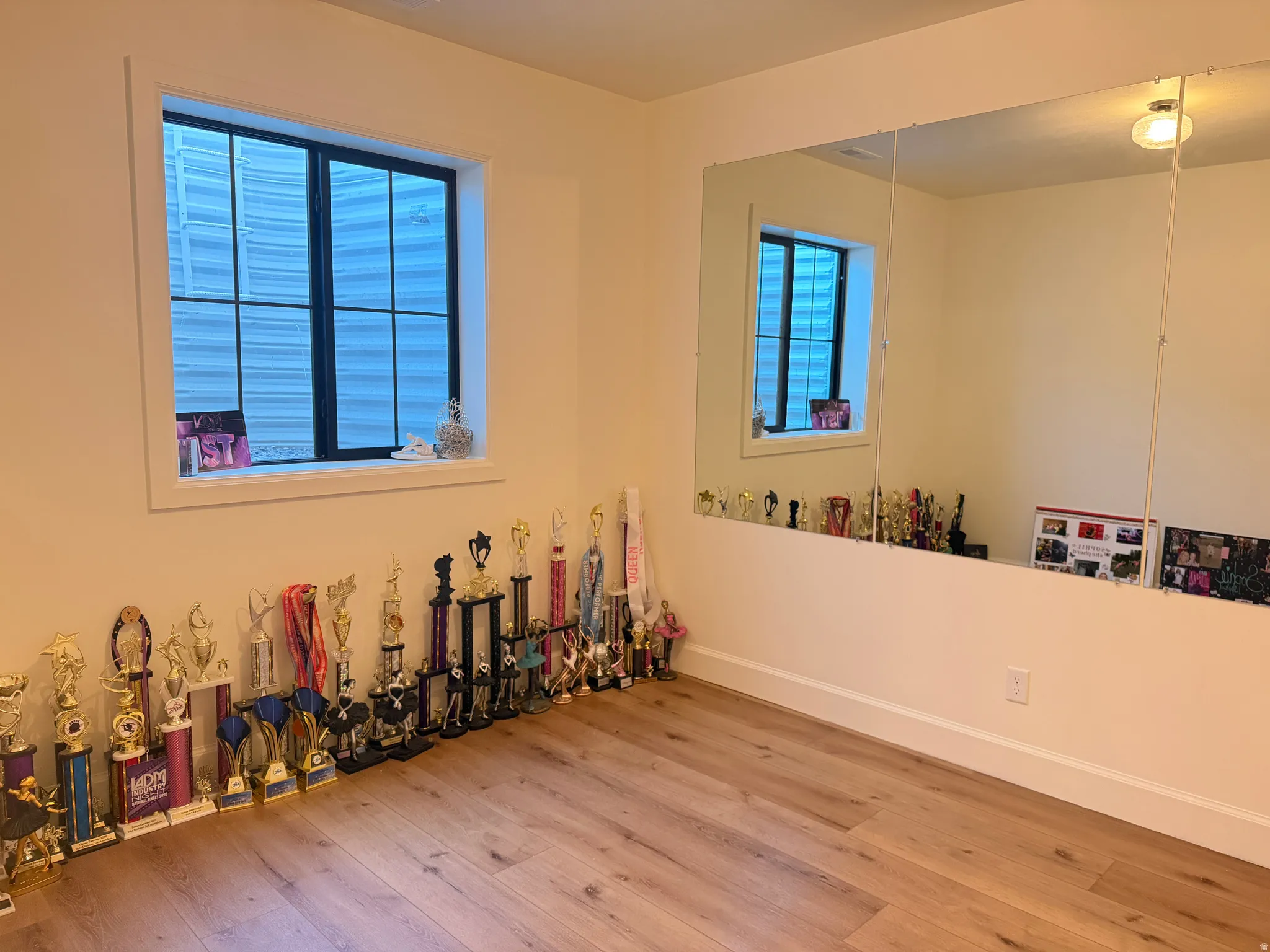 Dance Studio/Exercise room featuring wood-finish flooring, a built-in wall mirror, a recessed window with black framing, and neutral wall tones. This could be a 6th bedroom.