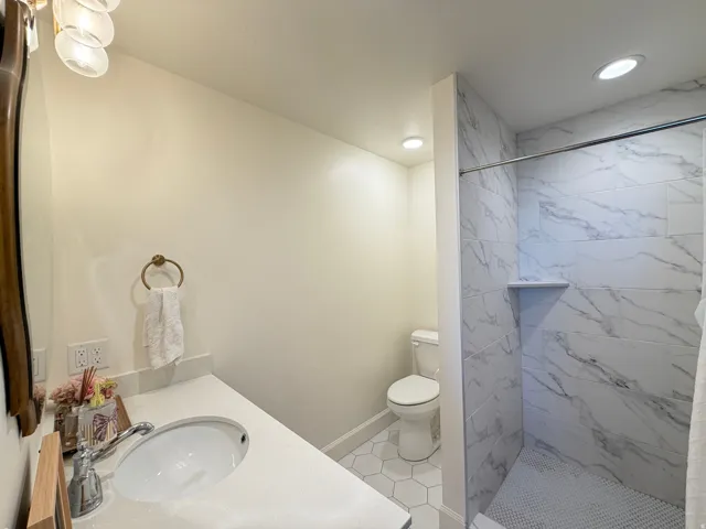 Bathroom featuring a walk-in shower with large format marble-look tile, a built-in shower niche, and a contrasting small mosaic tile shower pan