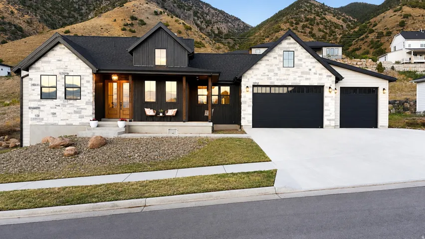 Timeless French  farmhouse exterior featuring light-colored stone and dark vertical siding with a 3-car garage and a covered porch.