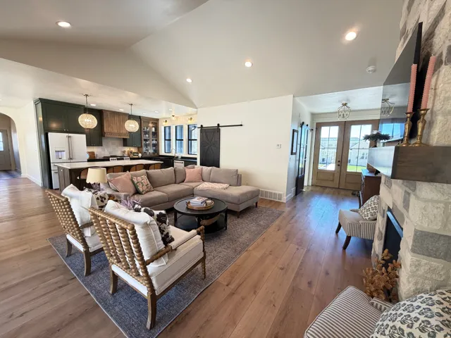 Open-concept living space featuring wood-finish flooring, a vaulted ceiling with recessed lighting, and a stone-clad fireplace with a wood mantel