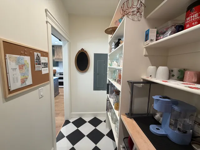 Walk in Pantry with an accent farm doorpace featuring black and white checkerboard flooring, built-in shelving, a dedicated counter area, and a doorway with detailed trim