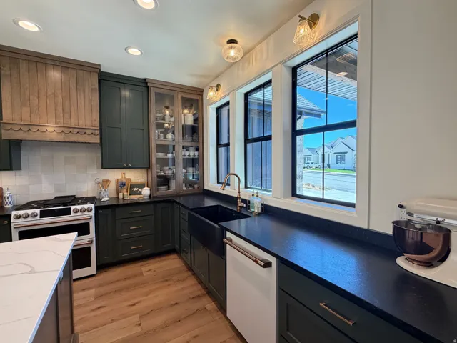 Gourmet kitchen featuring deep green cabinetry, wood-finish flooring, and a decorative wood range hood