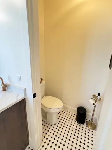 Powder room with black and white hexagonal floor tiling, a white toilet, and a vanity featuring a white countertop with grey veining