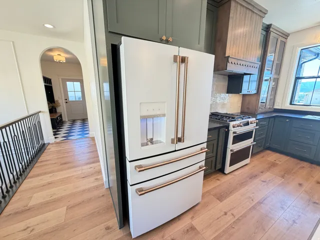 Modern kitchen featuring a white French door refrigerator with copper-toned hardware, dark cabinetry, and a built-in range with a double oven