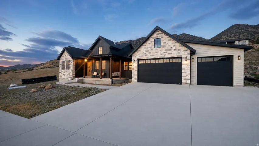 Timeless French  farmhouse exterior featuring light-colored stone and dark vertical siding with a 3-car garage and a covered porch. Large concrete drive way.