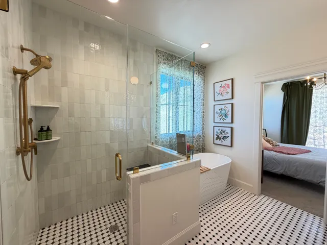 Primary bathroom featuring a freestanding soaking tub, a walk-in shower with clear glass enclosure and gold-finish fixtures, and distinctive black and white patterned floor tiling and walking closet
