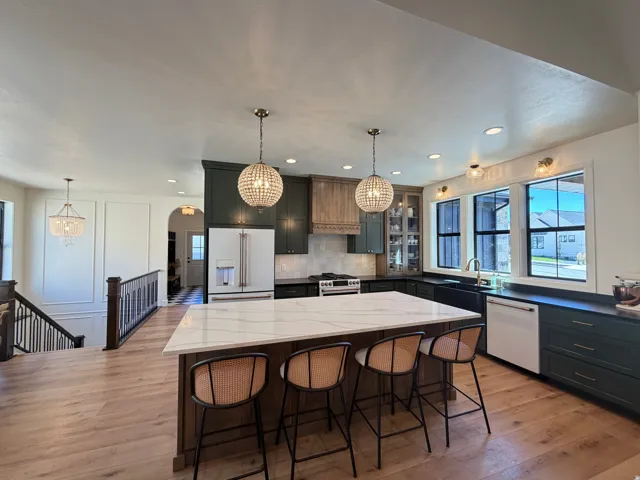 Kitchen featuring a large central island with seating, pendant lighting, wood-finish flooring, and two-tone cabinetry