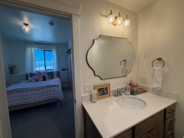 Bathroom part of bathroom/bedroom suite. Vanity featuring a white countertop with an undermount sink, brass hardware, and a decorative framed mirror