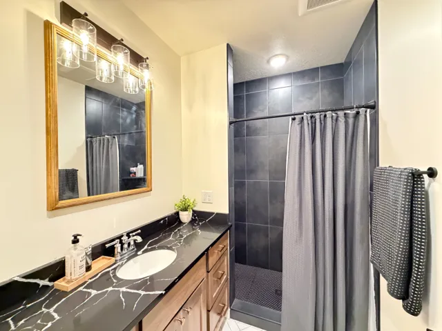 Bathroom featuring a full vanity with an undermount sink, a dark countertop with white veining, wood-finish cabinetry, and a gold-framed mirror