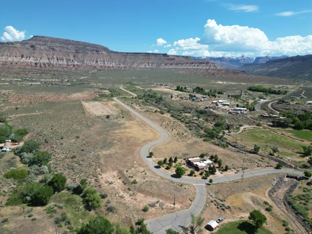 Expansive desert landscape featuring a residential property with a paved road system, surrounded by natural vegetation, and framed by distant mountain ranges