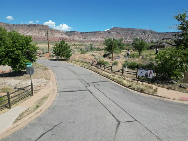 Paved roadway bordered by sidewalks and a natural landscape, featuring distant mesa formations
