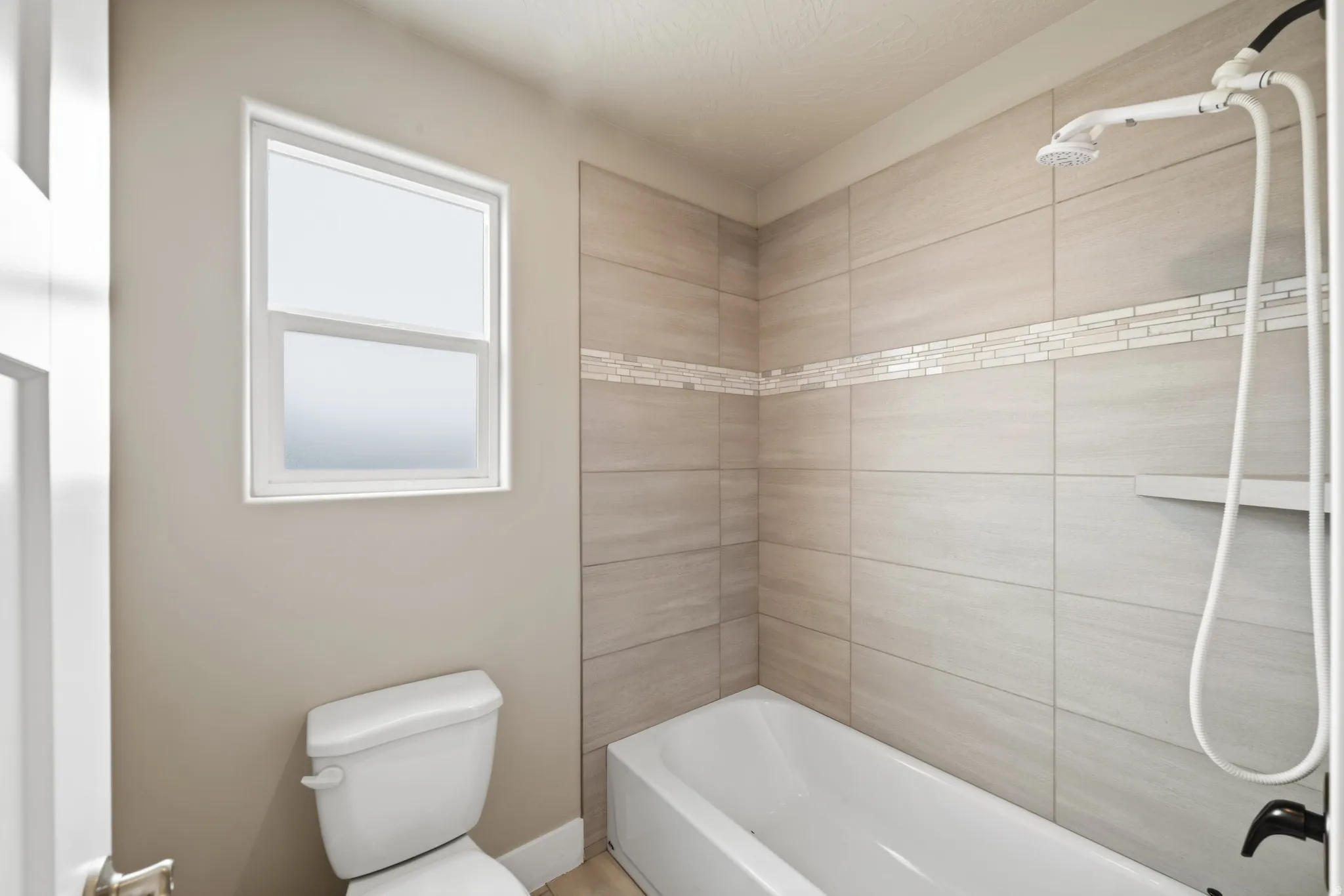 Bathtub and shower combination featuring neutral-toned rectangular wall tiles with a decorative mosaic accent band