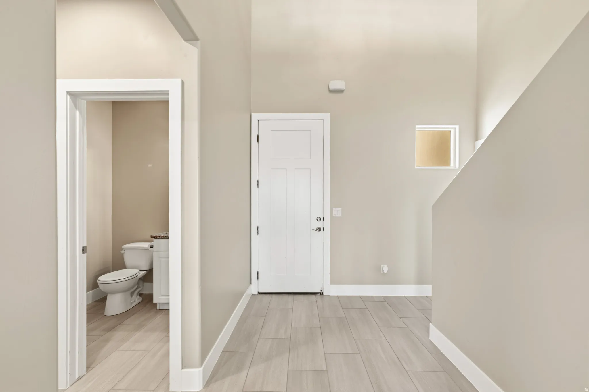 Entryway featuring wood-finish flooring, a contemporary white door, and a conveniently located powder room with a white vanity and toilet