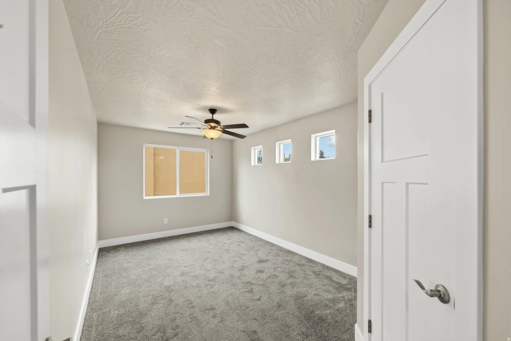 Spacious room featuring neutral-toned walls, grey carpet, and a ceiling fan