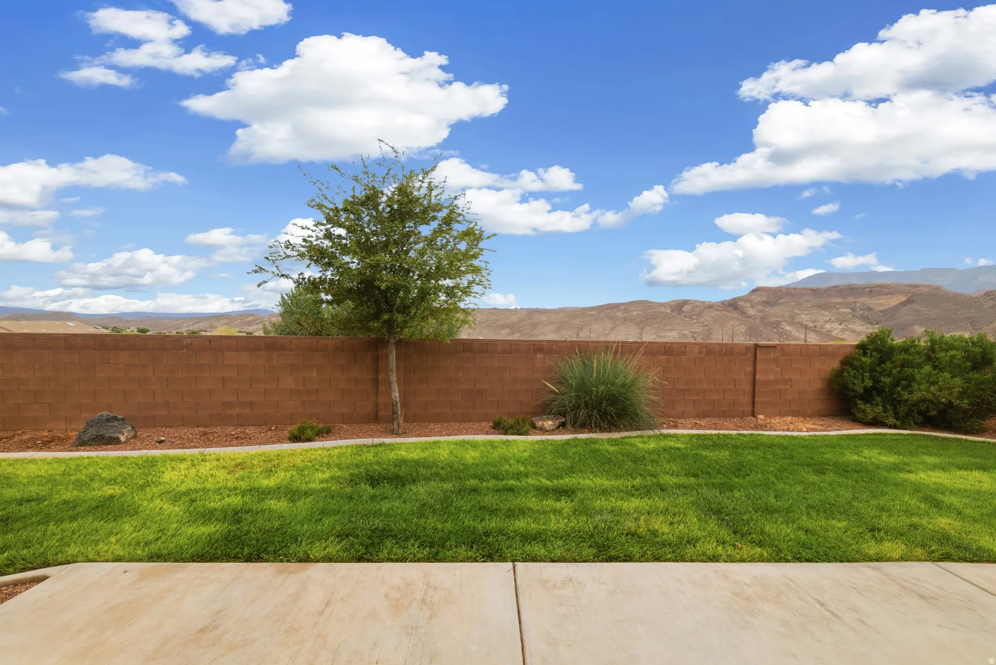 Patio area featuring concrete slab, green lawn, a block fence, and distant mountainous terrain