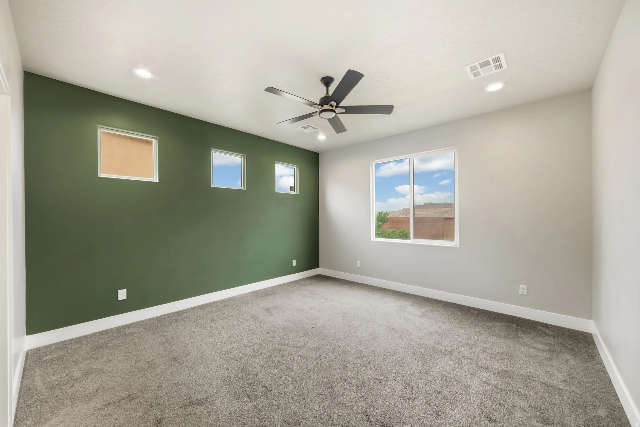 Spacious room featuring plush gray carpeting and a bold green accent wall