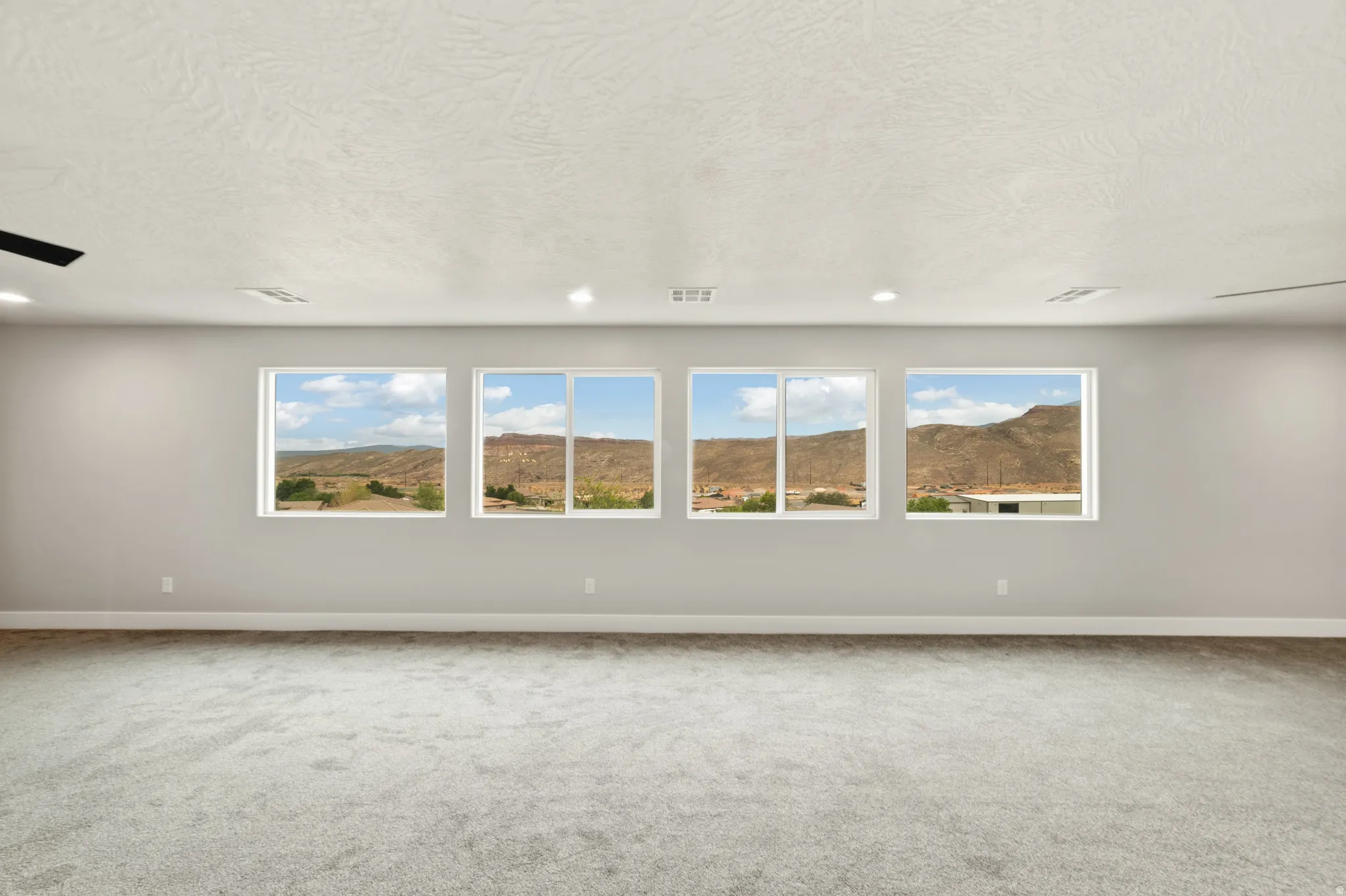 Spacious room featuring four large windows, grey wall paint, plush carpet flooring, and recessed ceiling lighting