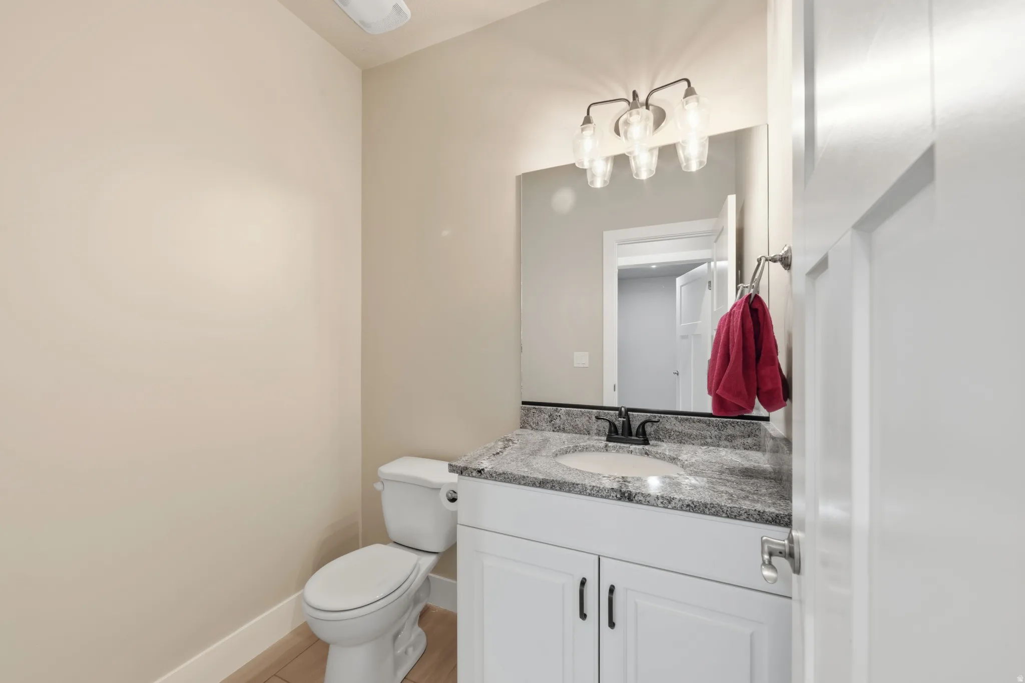 Bathroom with a white vanity featuring shaker-style cabinetry and dark hardware, a granite-finish countertop with an undermount sink, and a wall-mounted mirror