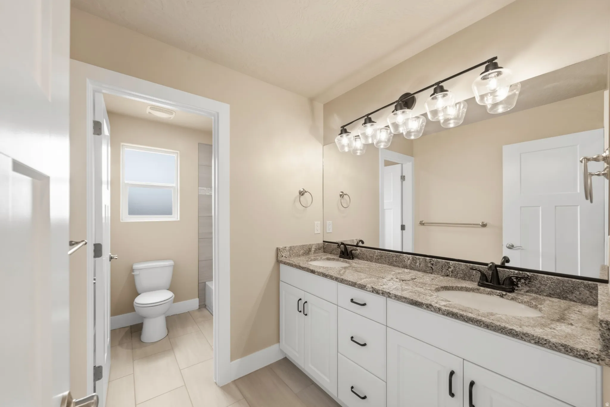 Bathroom featuring a dual vanity with a granite-finish countertop, white cabinetry, and matte black fixtures