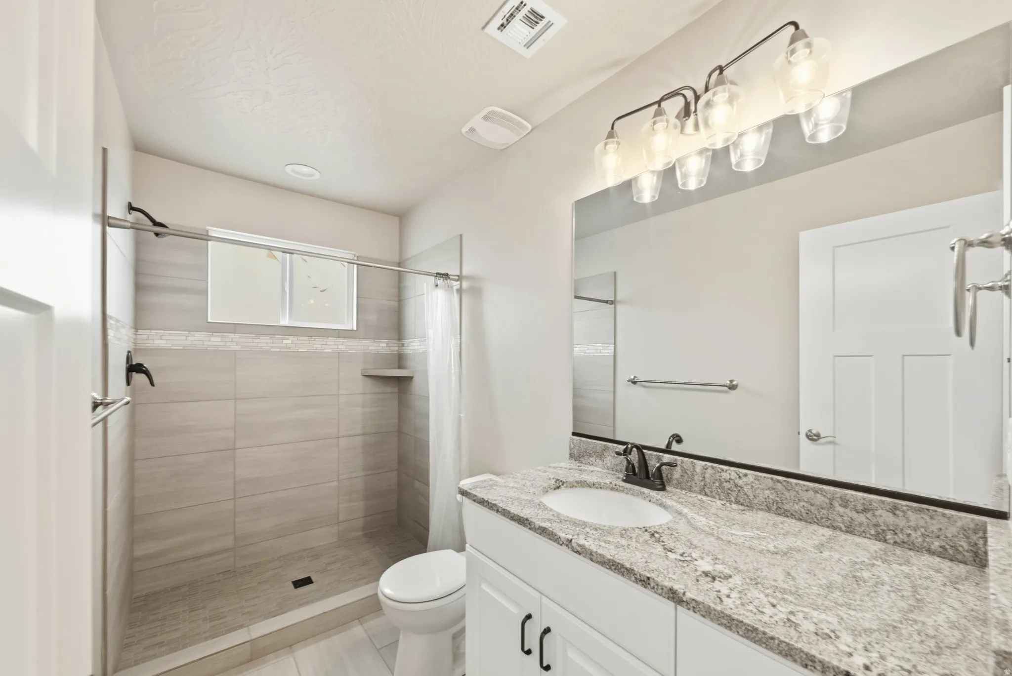 Bathroom featuring a walk-in shower with light grey tile surround, decorative mosaic tile accent, and built-in shelf