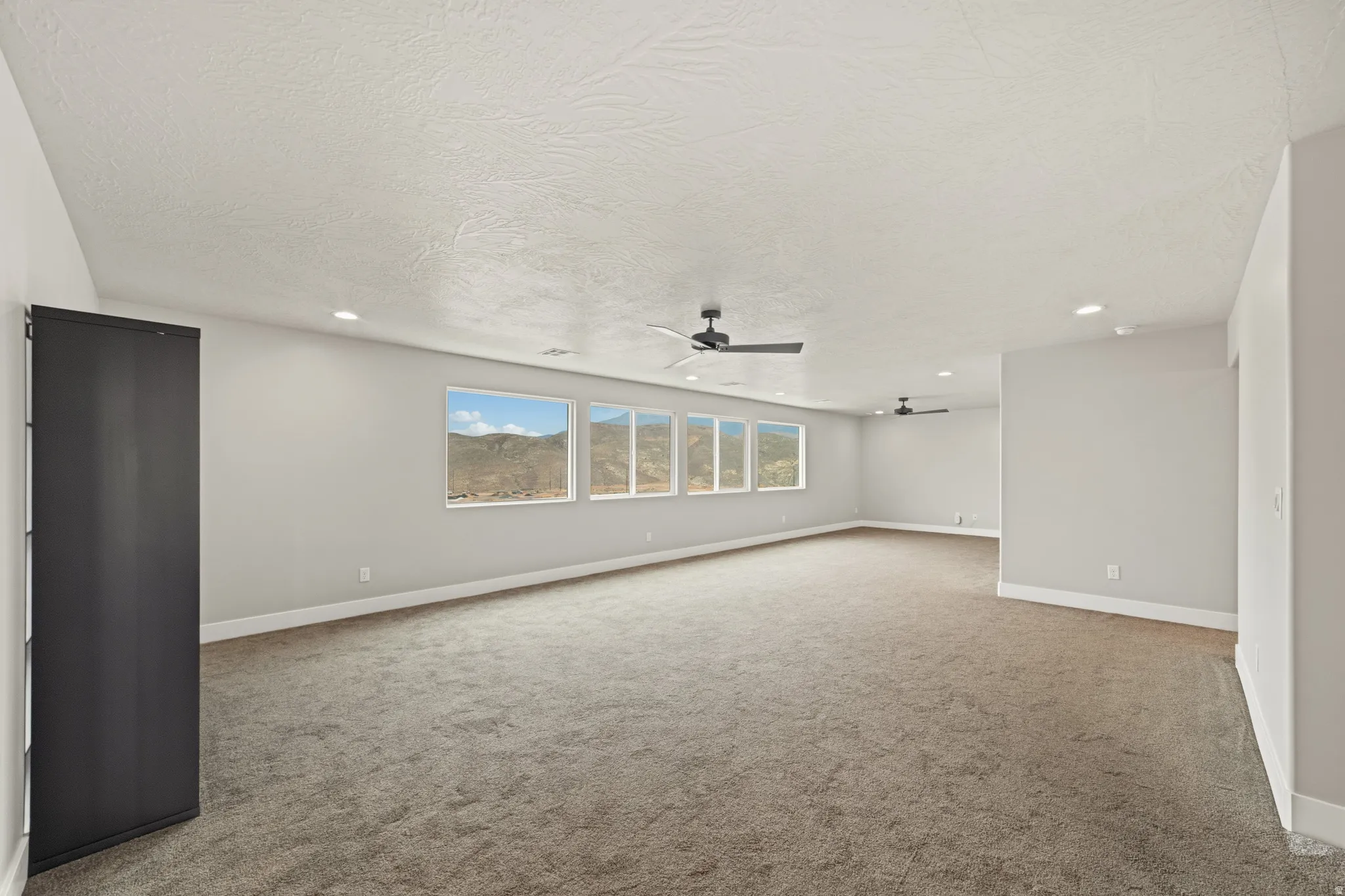 Spacious room featuring multiple horizontal windows, recessed lighting, two ceiling fans, gray carpeting, and baseboard molding